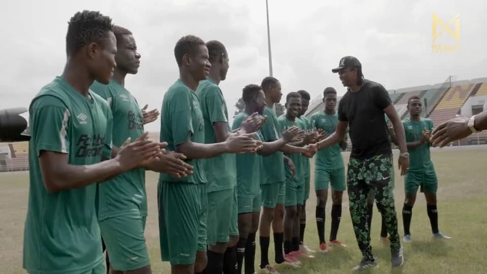 A line of players in Football Dreamz shirts shaking hands with a coach on a pitch